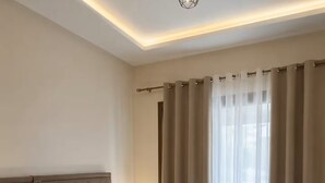 Habitación de hotel moderna con una cama grande, una mesita de noche, una lámpara y vistas al exterior a través de cortinas traslúcidas.