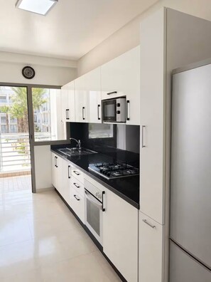 A modern kitchen with white cabinets, a black countertop, and stainless steel appliances. - Bouznika Beach: 2-bedroom with a pool (Bouznika)