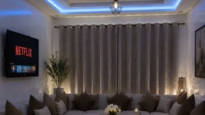 Una sala de estar moderna con un sofá seccional, una mesa de centro, un televisor mostrando Netflix e iluminación ambiental.