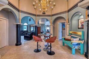 Eine geräumige Lobby mit einem Kronleuchter, einem runden Tisch mit Stühlen und einer Bank mit Kissen.