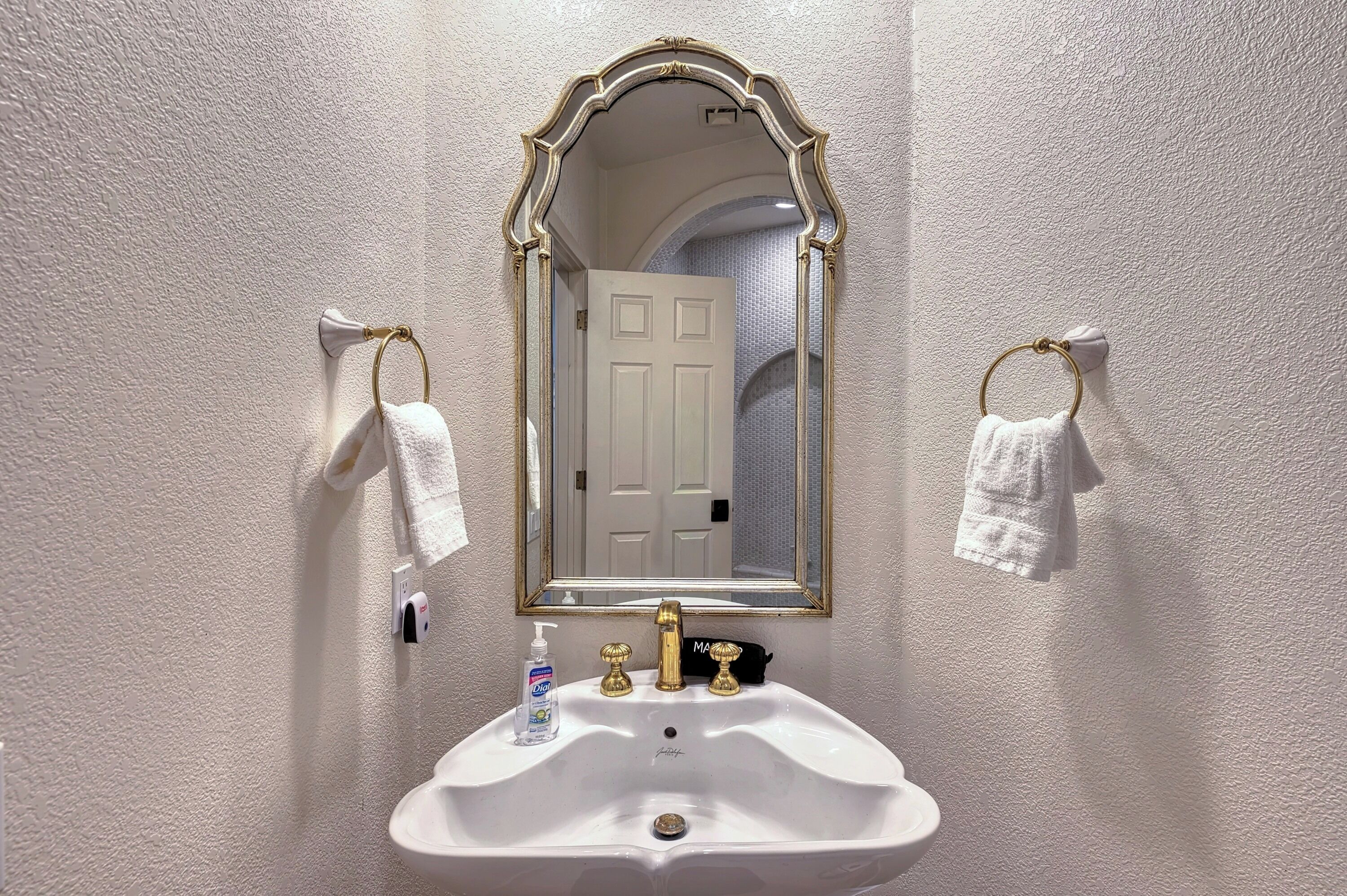 Ein Badezimmer mit einem weißen Waschbecken, einem Spiegel mit goldener Rahmung und zwei Handtüchern, die an Handtuchhaltern hängen.