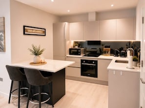 A modern kitchen with a dining area, featuring a built-in oven, microwave, and a small island with bar stools. - Modern 1BD Flat l Gated Parking l Contractors (Surrey)