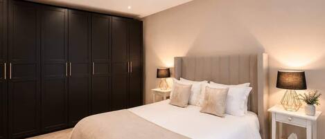 A bedroom with a large bed, dark wardrobe, bedside tables with lamps, and a neutral color scheme.