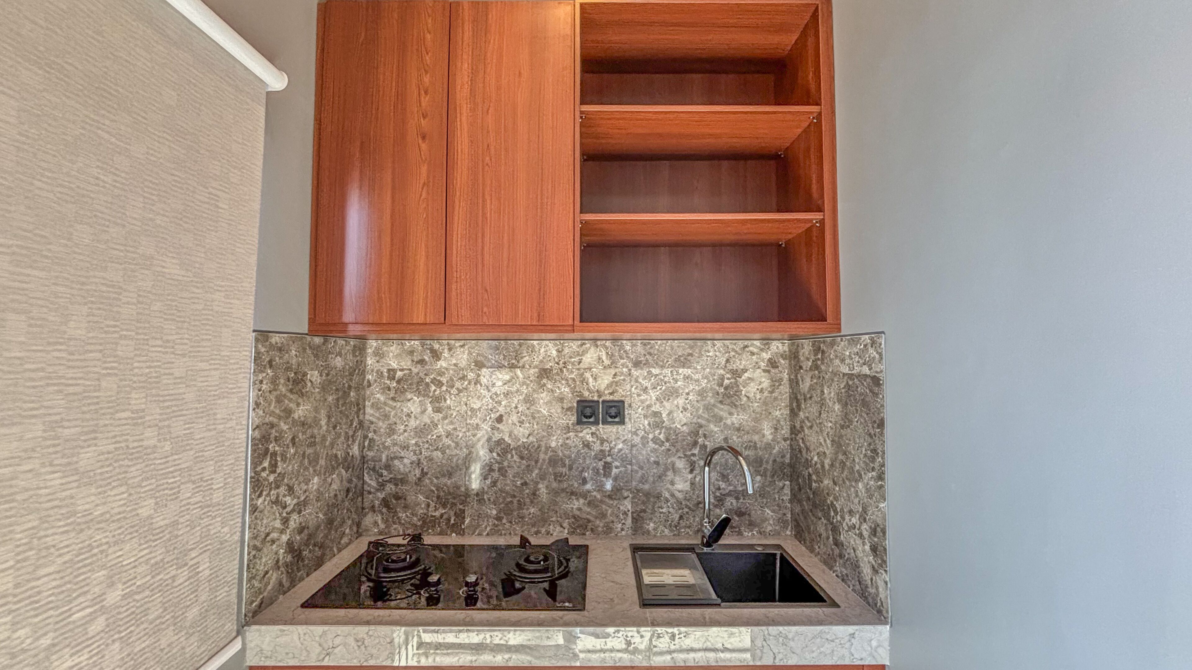 A kitchen with a marble backsplash, wooden cabinets, and a stainless steel sink.