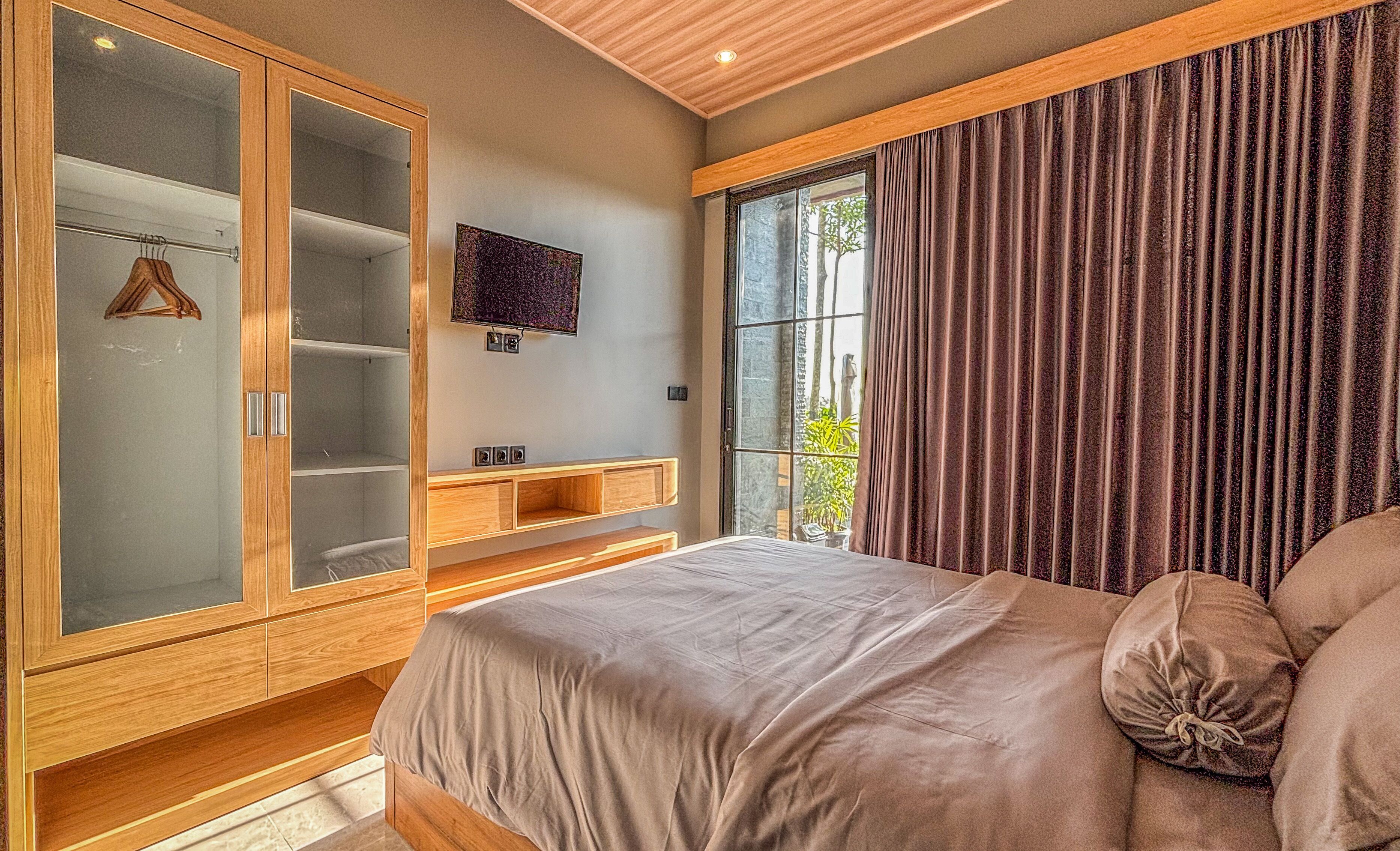 A bedroom with a bed, a wardrobe, a TV, and a window with curtains.