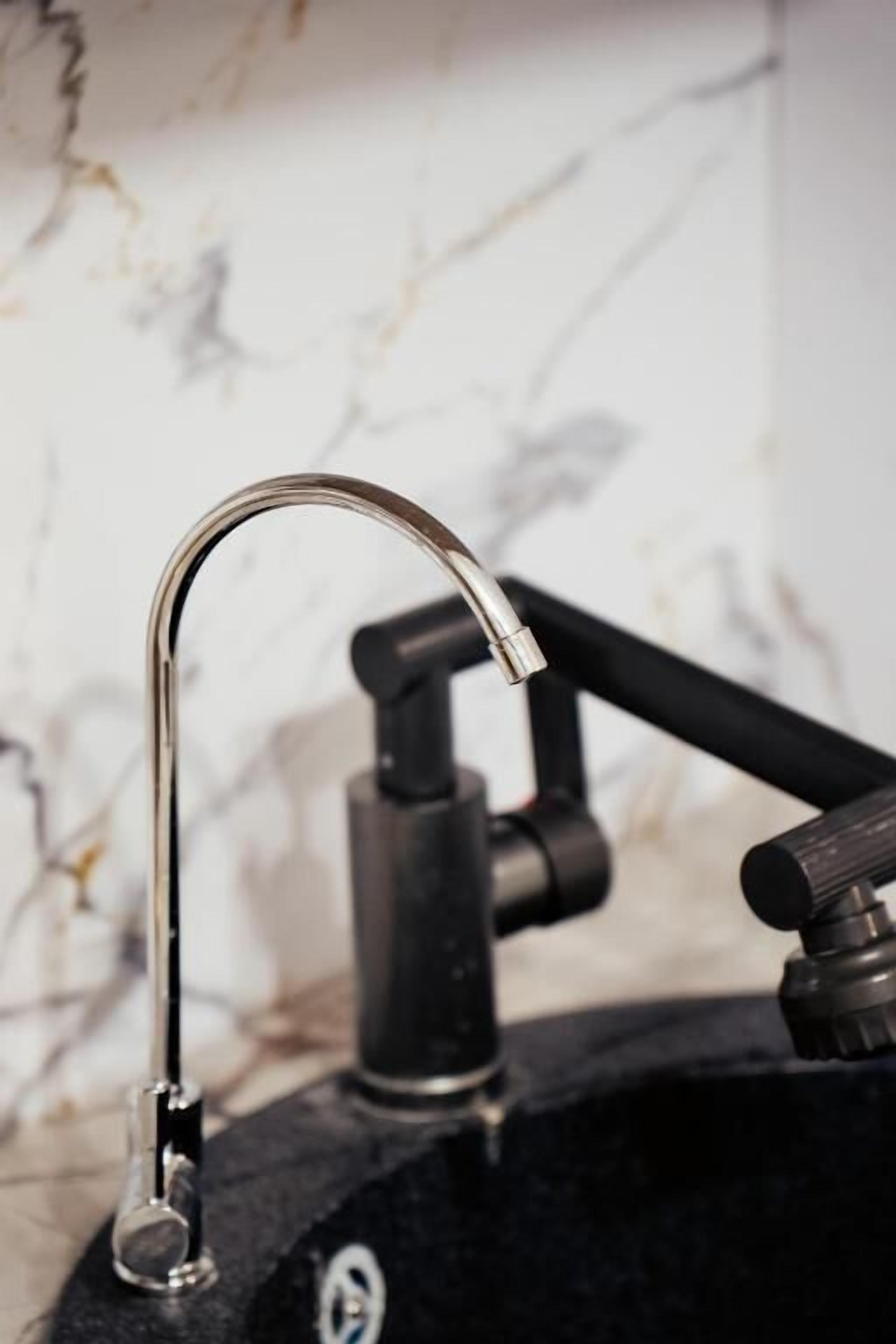 A kitchen sink with a modern faucet, a black countertop, and a marble backsplash.