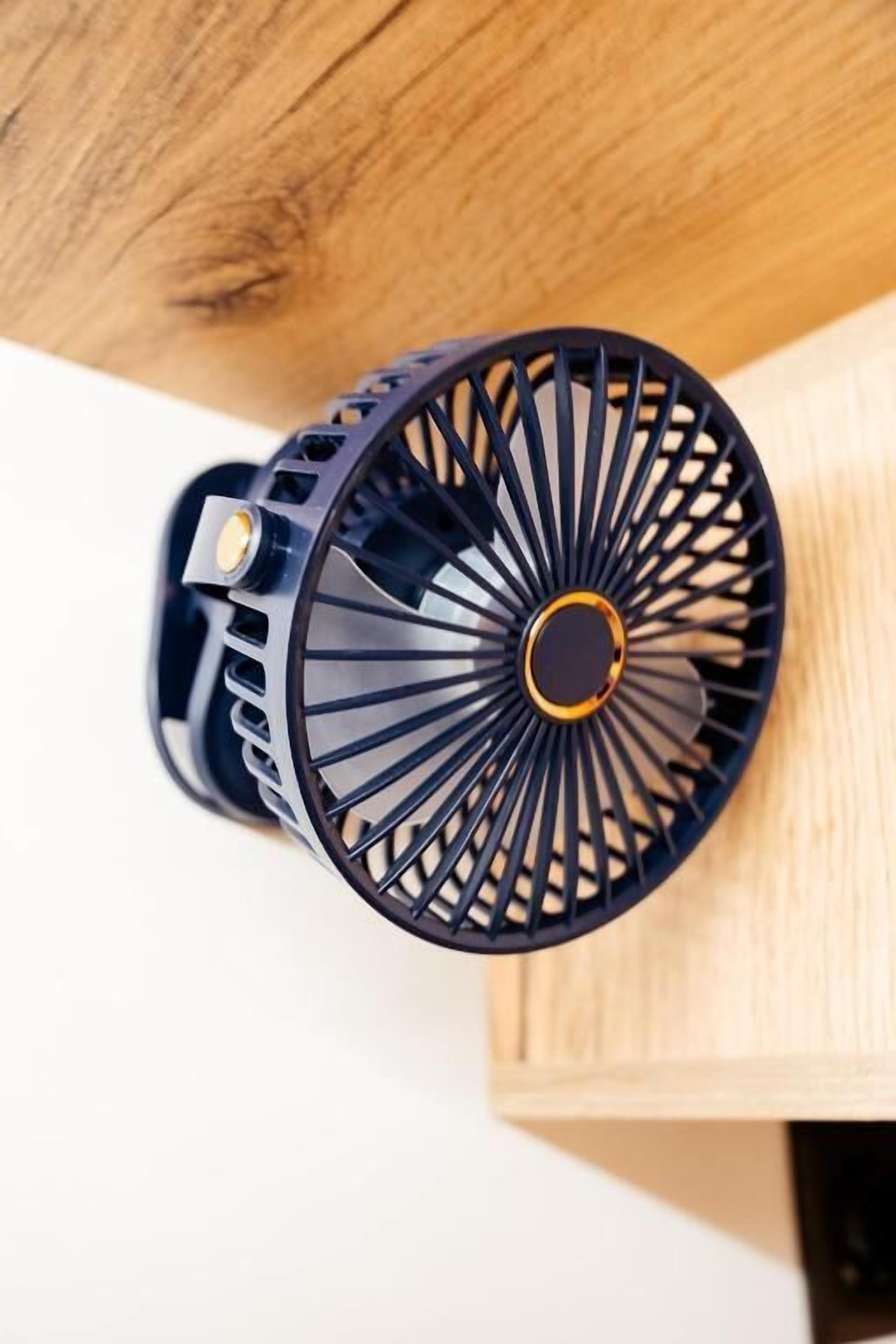 Un abanico negro con diseño circular y una perilla central, sobre una superficie de madera.