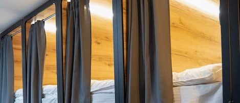 A row of bunk beds with curtains, wooden walls, and a tiled floor.