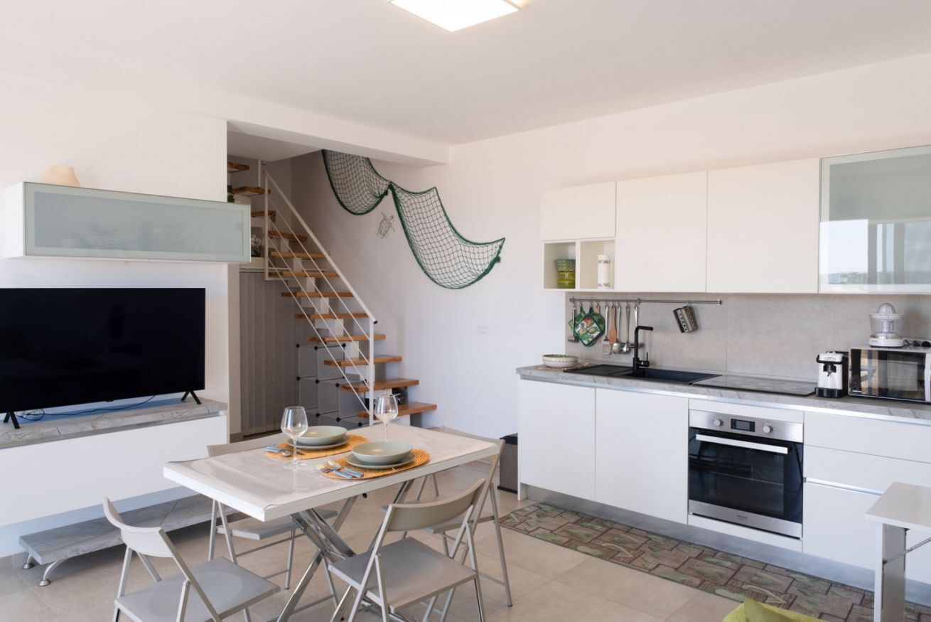 A modern kitchen with white cabinets, a built-in oven, and a dining area with a table and chairs.
