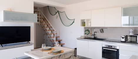A modern kitchen with white cabinets, a built-in oven, and a dining area with a table and chairs.