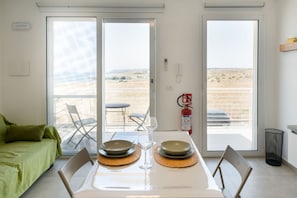 Ein Zimmer mit Esstisch für zwei Personen, einem grünen Sofa und Blick auf die Wüste durch große Schiebetüren.
