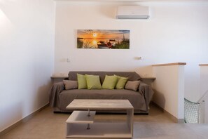 Ein Zimmer mit einer Couch, einem Couchtisch, einer Klimaanlage und einem Gemälde mit Sonnenuntergang über Wasser.