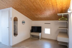 Ein Zimmer mit Holzboden, einem Fernseher auf einem Schrank, einer Tür und einem Fenster.