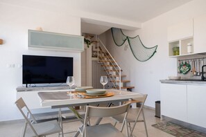A modern kitchen with a dining area, a TV, and a staircase. - Green Oasi 1 Marzamemi  (Marzamemi)