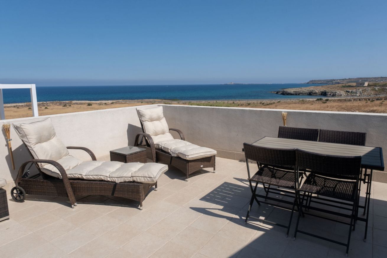 A terrace with wicker furniture, a table, and a view of the sea.