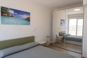 Ein Schlafzimmer mit Bett, Schreibtisch, Stuhl, Kleiderschrank und einem großen Fenster mit Blick.