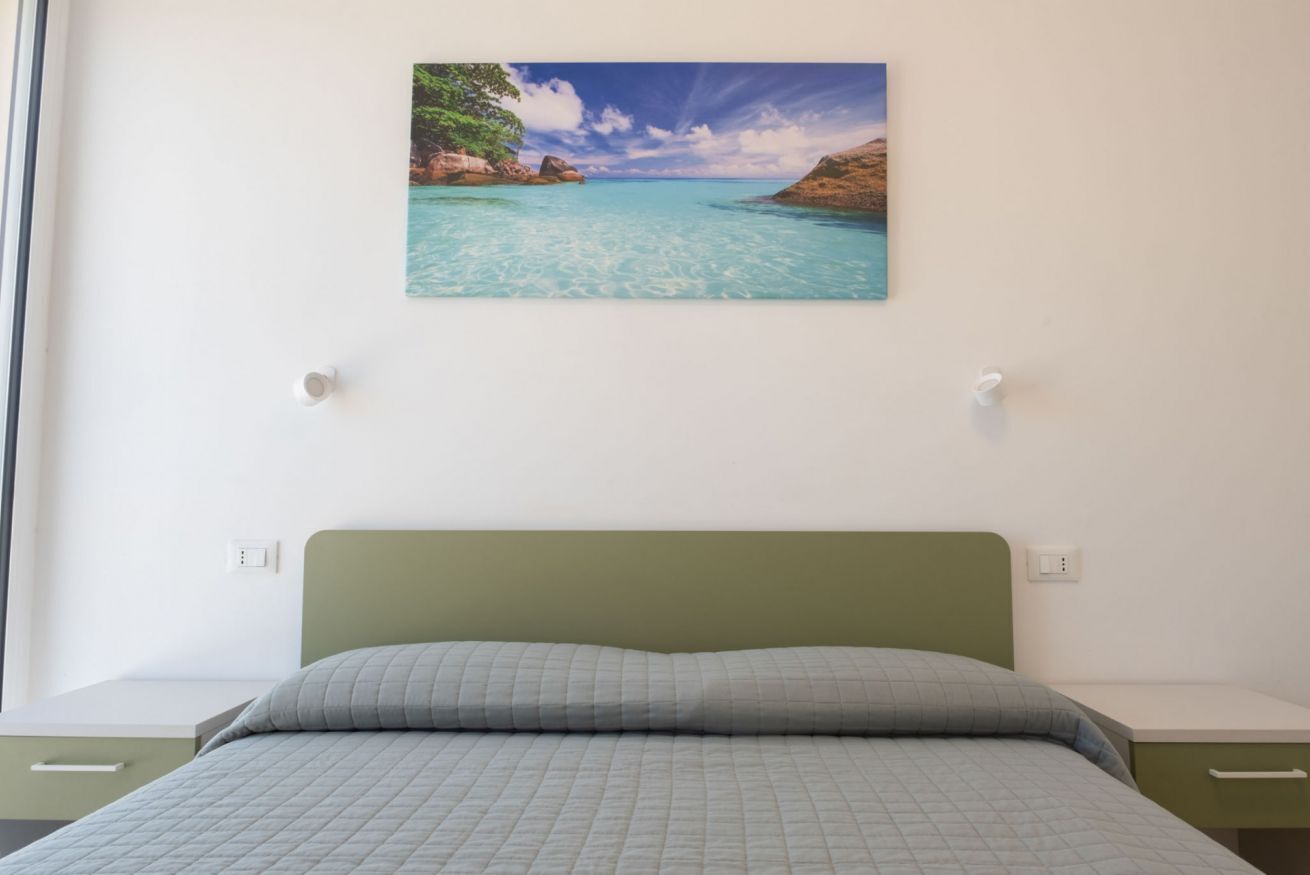 Un dormitorio con cama, un cuadro colgado en la pared de una playa y una ventana.