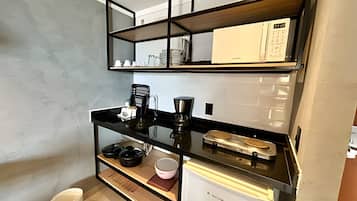 Cocina compacta con encimera negra, cafetera, tostadora y un refrigerador pequeño.