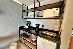 Cocina compacta con encimera negra, cafetera, tostadora y un refrigerador pequeño.