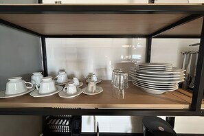 Una estantería de cocina con vajillas de cerámica blanca, vasos de vidrio y platos blancos apilados.