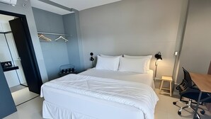 Een moderne hotelkamer met een groot bed, een bureau met stoel, een kledingkast en een nachtkastje met lamp.
