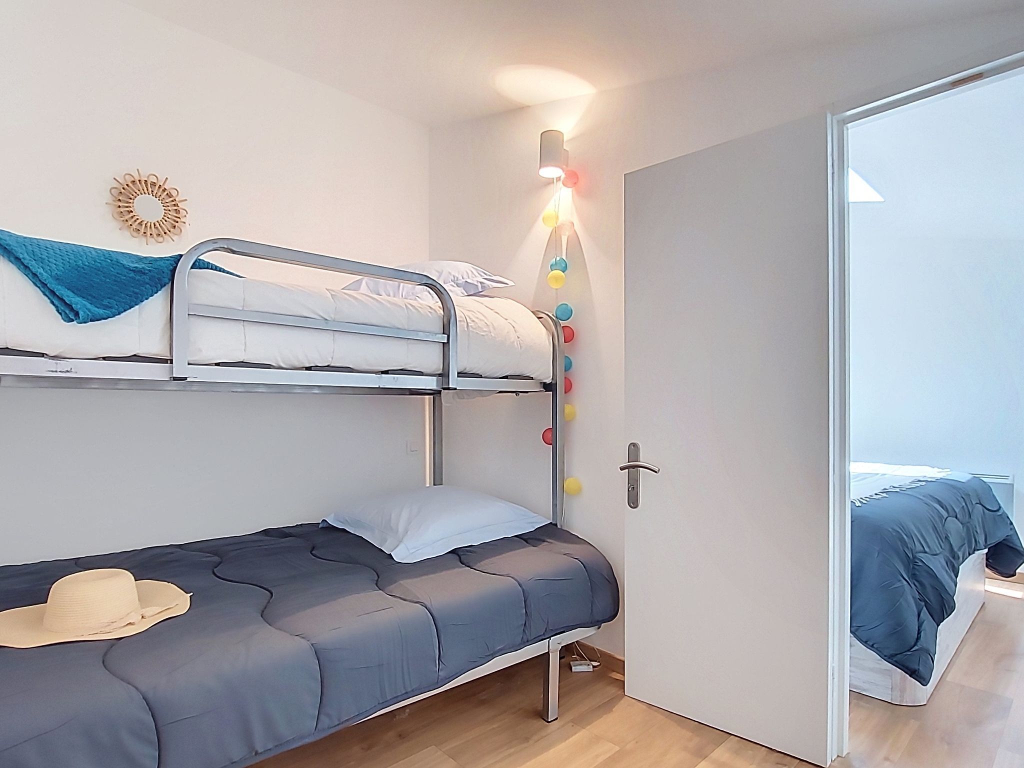 Habitación con literas, una puerta, una lámpara en la pared y un sombrero sobre la cama.