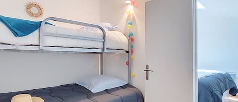 Habitación con literas, una puerta, una lámpara en la pared y un sombrero sobre la cama.