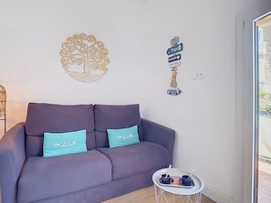 A modern living room with a grey sofa, teal cushions, a decorative wall piece, and a small table with a tray. - Les Embruns by Interhome (Sainte Maxime)
