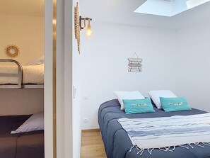 A bedroom with a bunk bed, a bed with teal pillows, a wall-mounted light fixture, and a small decorative item. - Les Embruns by Interhome (Sainte Maxime)