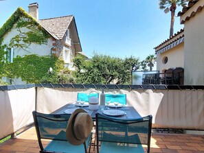 An outdoor patio with a table set for two, a hat, and a bottle, surrounded by a white fence and buildings in the background. - Les Embruns by Interhome (Sainte Maxime)