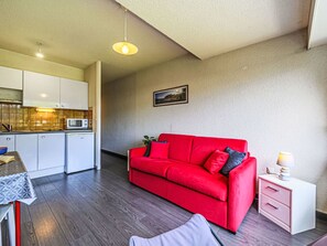 A compact living space with a kitchenette, a red sofa, a bedside table, and a small bedside lamp. - Les Alizés by Interhome (Carnac)