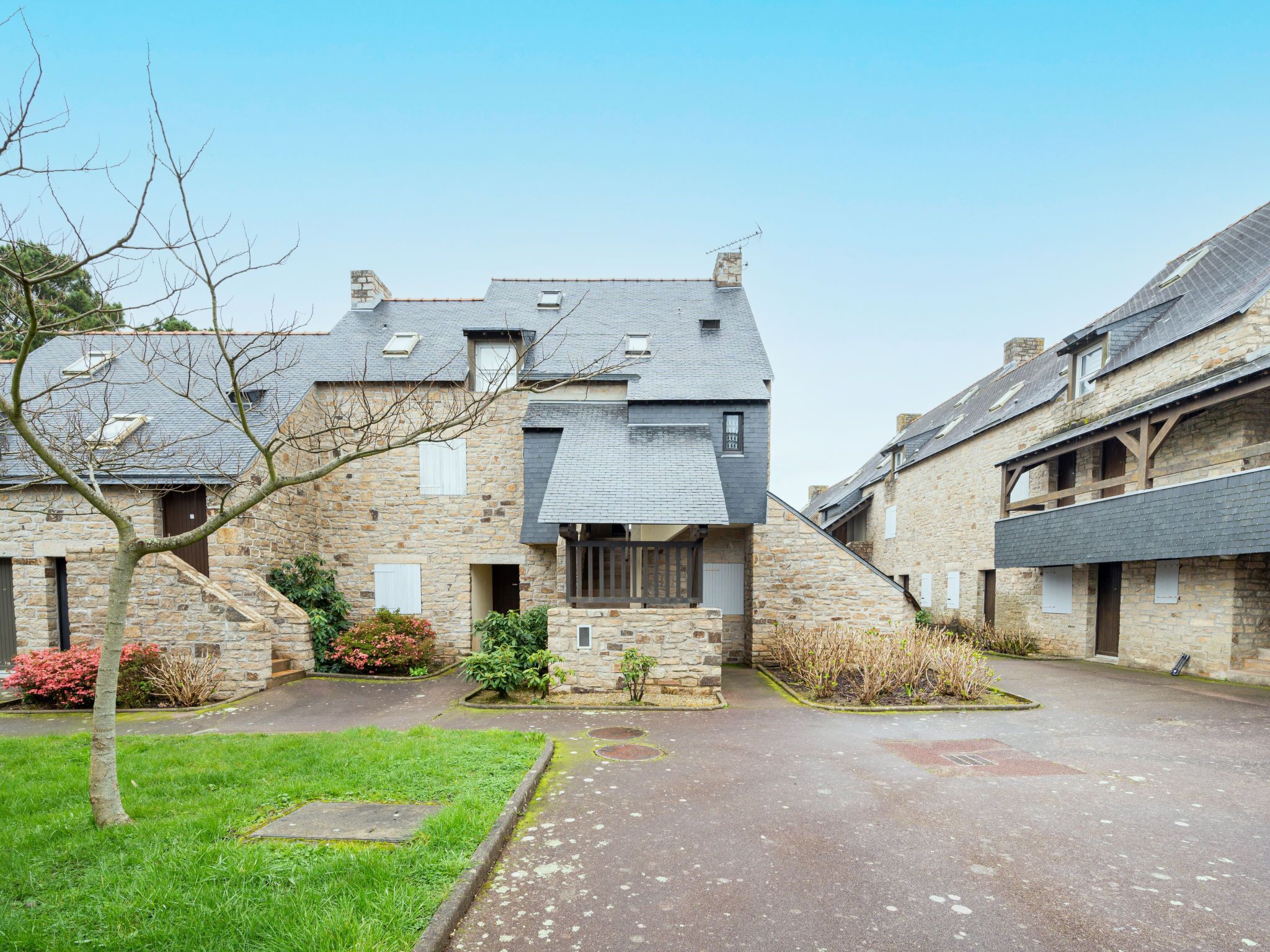 A stone building with a sloped roof, a small garden, and a paved driveway.