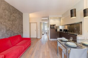 A modern living area with a red sofa, a dining table set with plates and glasses, and a kitchen with stainless steel appliances. - Torino Centro | Casa Gran Madre (Torino)