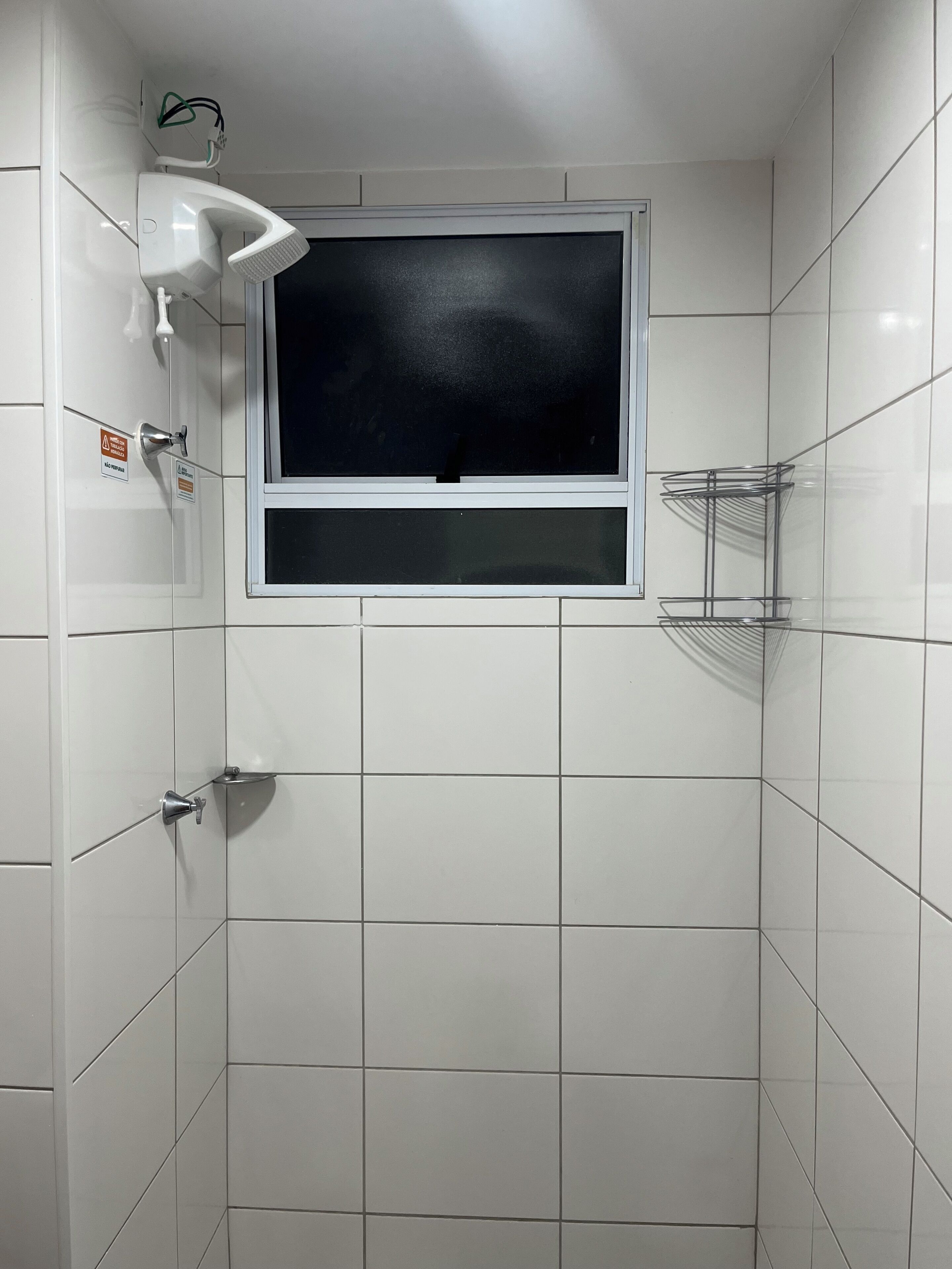 A bathroom with white tiles, a window, a showerhead, and a towel rack.