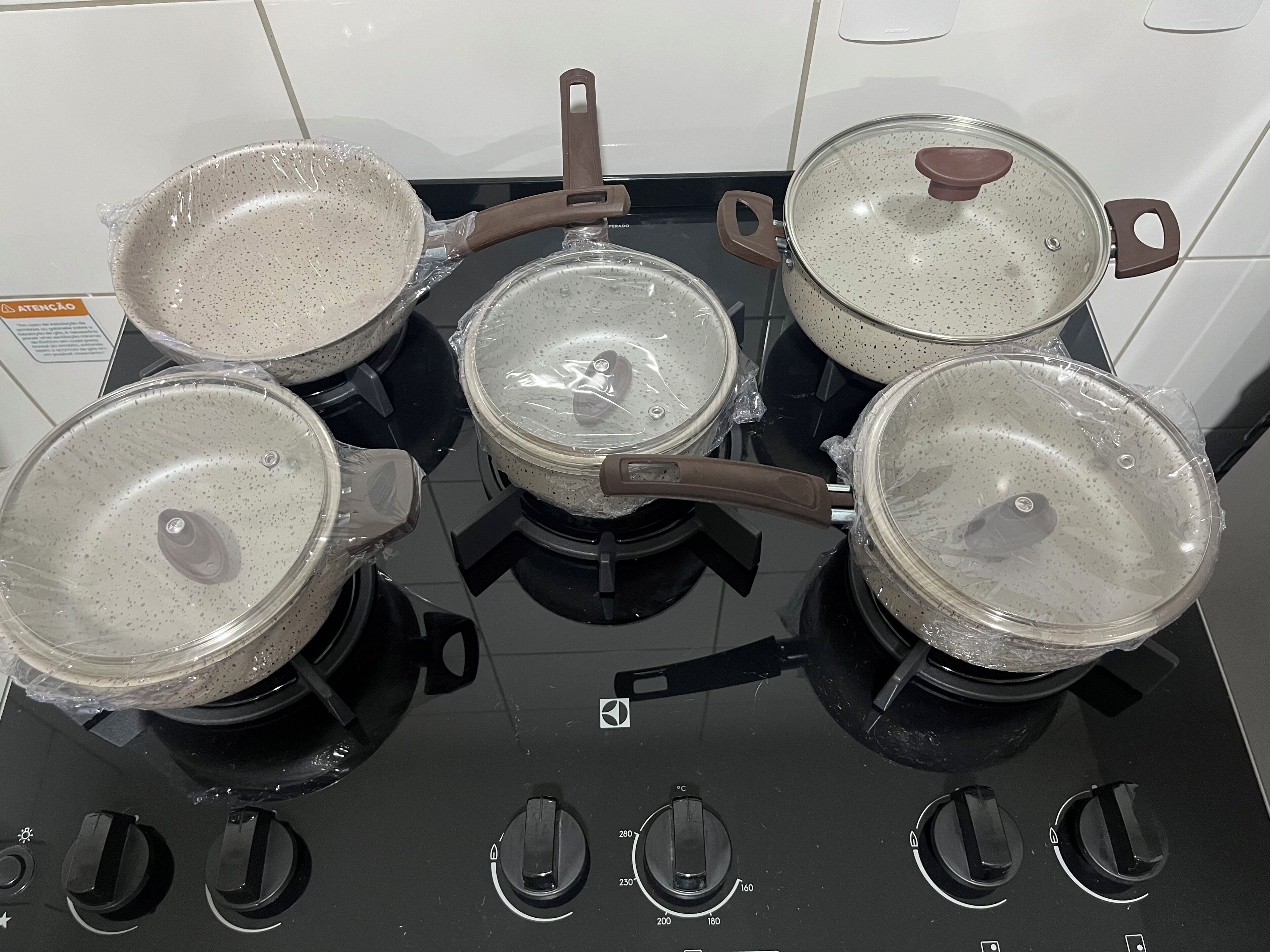 A kitchen stove with four pots and pans, a control panel with temperature settings, and a warning label.