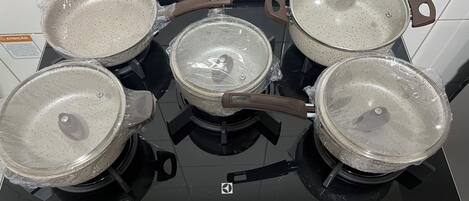 A kitchen stove with four pots and pans, a control panel with temperature settings, and a warning label.