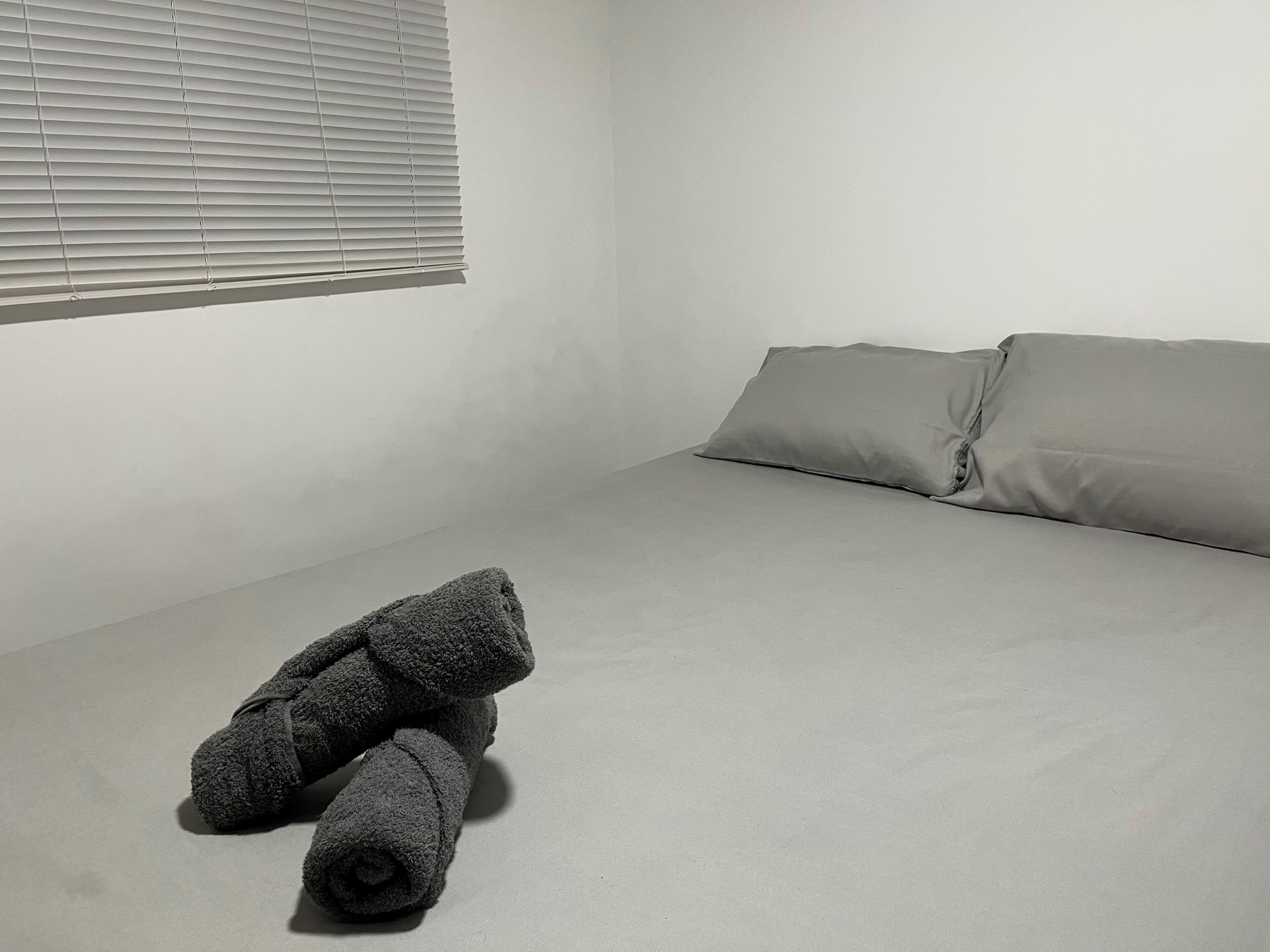 Habitación minimalista con cama, almohadas y una toalla enrollada.