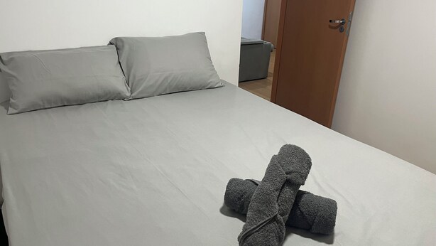 A neatly made bed with grey linens and a folded towel on the bed. - Apartment 15 minutes from Confins International Airport (Lagoa Santa)
