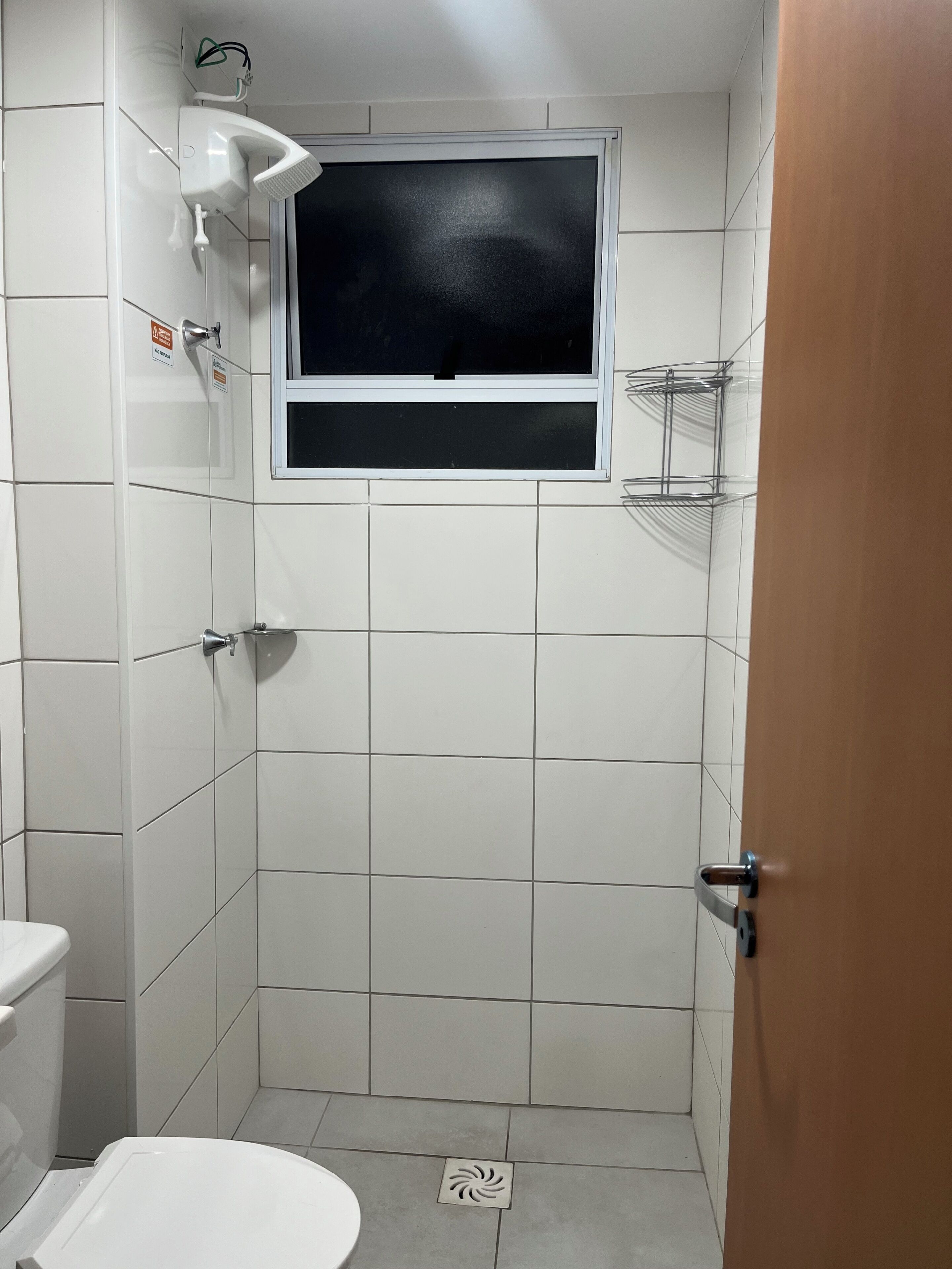 A small, tiled bathroom with a toilet, a shower, and a window.