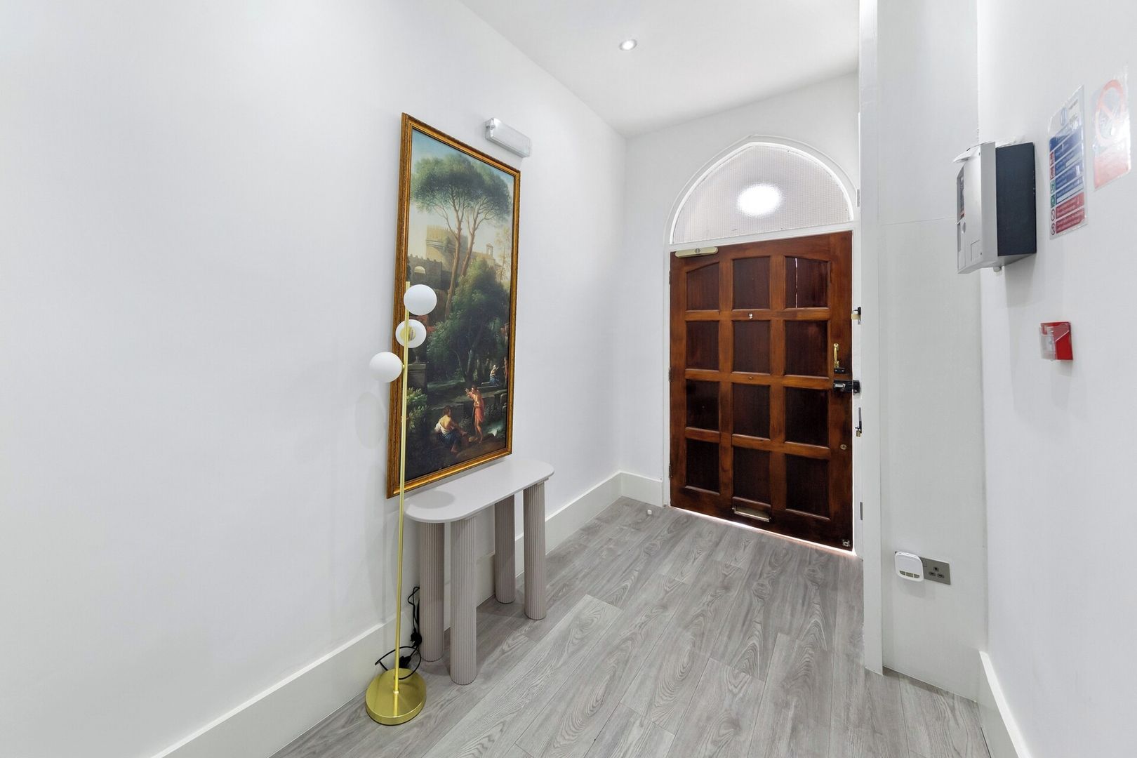 A hallway with a wooden door, a painting on the wall, and a floor lamp.