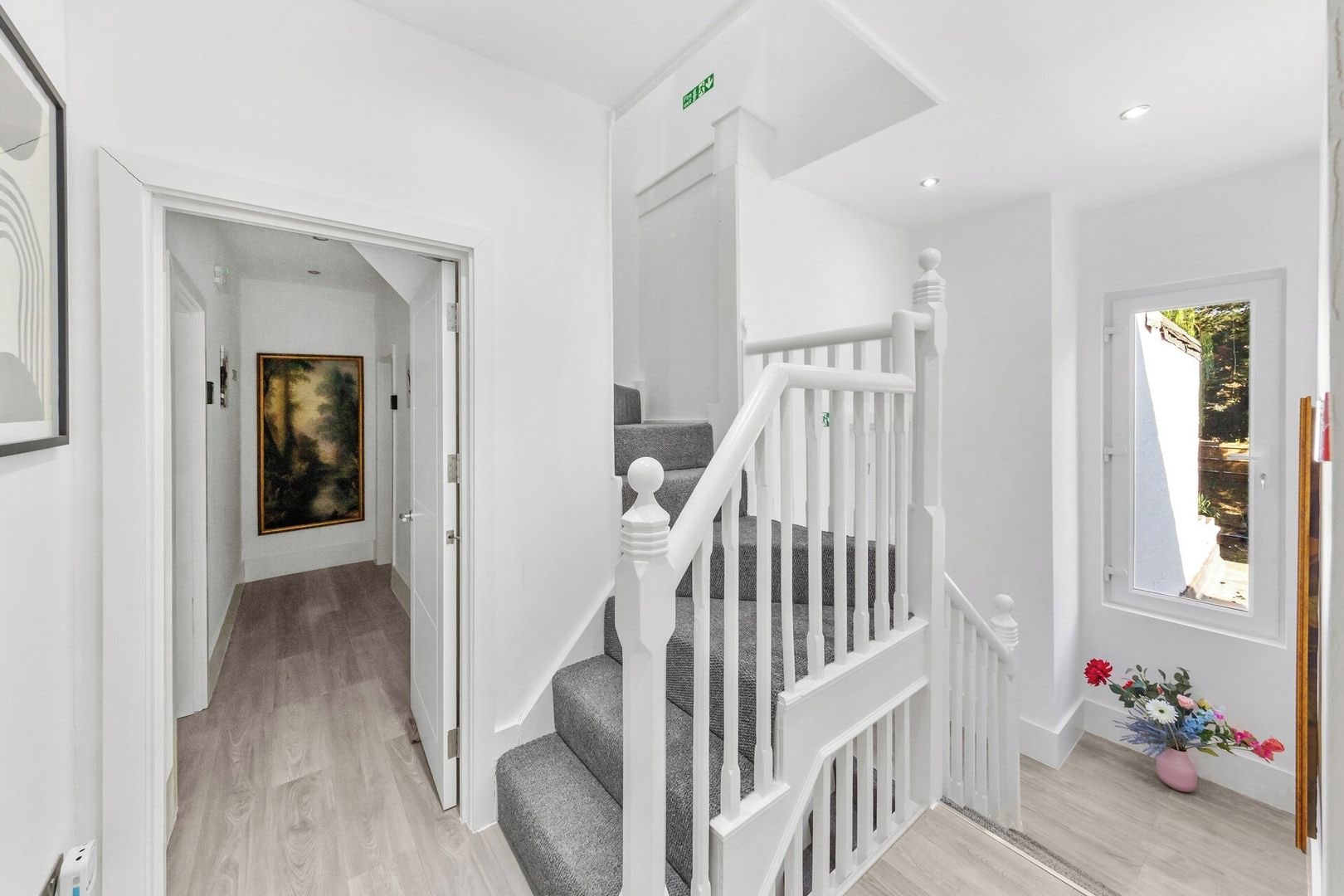 A hallway with a staircase, a painting, and a window with flowers.