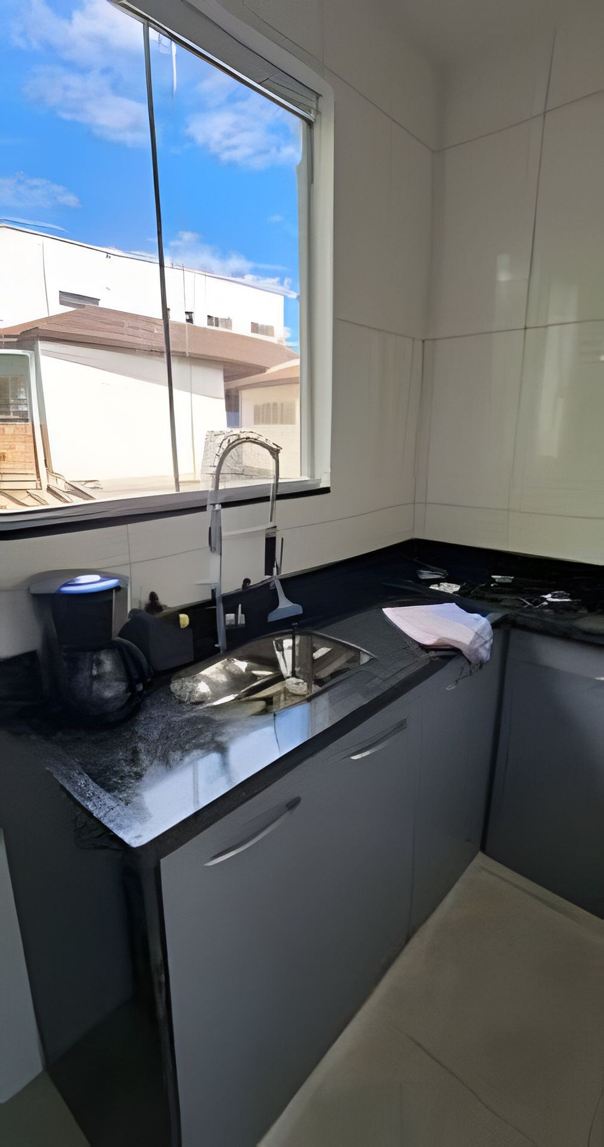 Uma cozinha com janela, pia, bancada e armários.