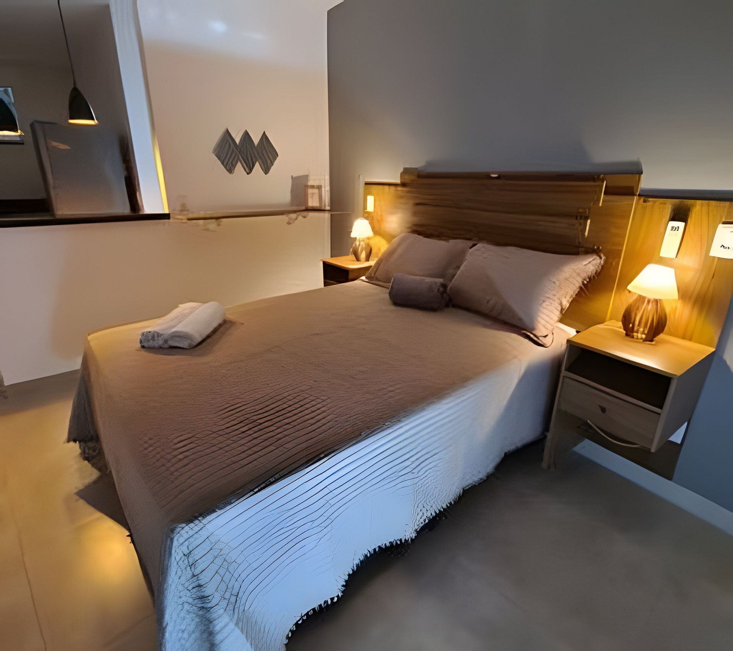 Un lit bien fait, avec une couverture, deux tables de chevet avec des lampes et un luminaire fixé au mur.