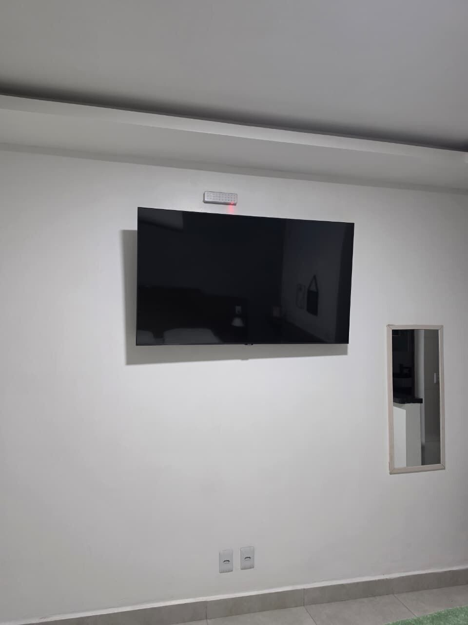 A room with a mounted flat-screen TV, a door, and a light switch on the wall.