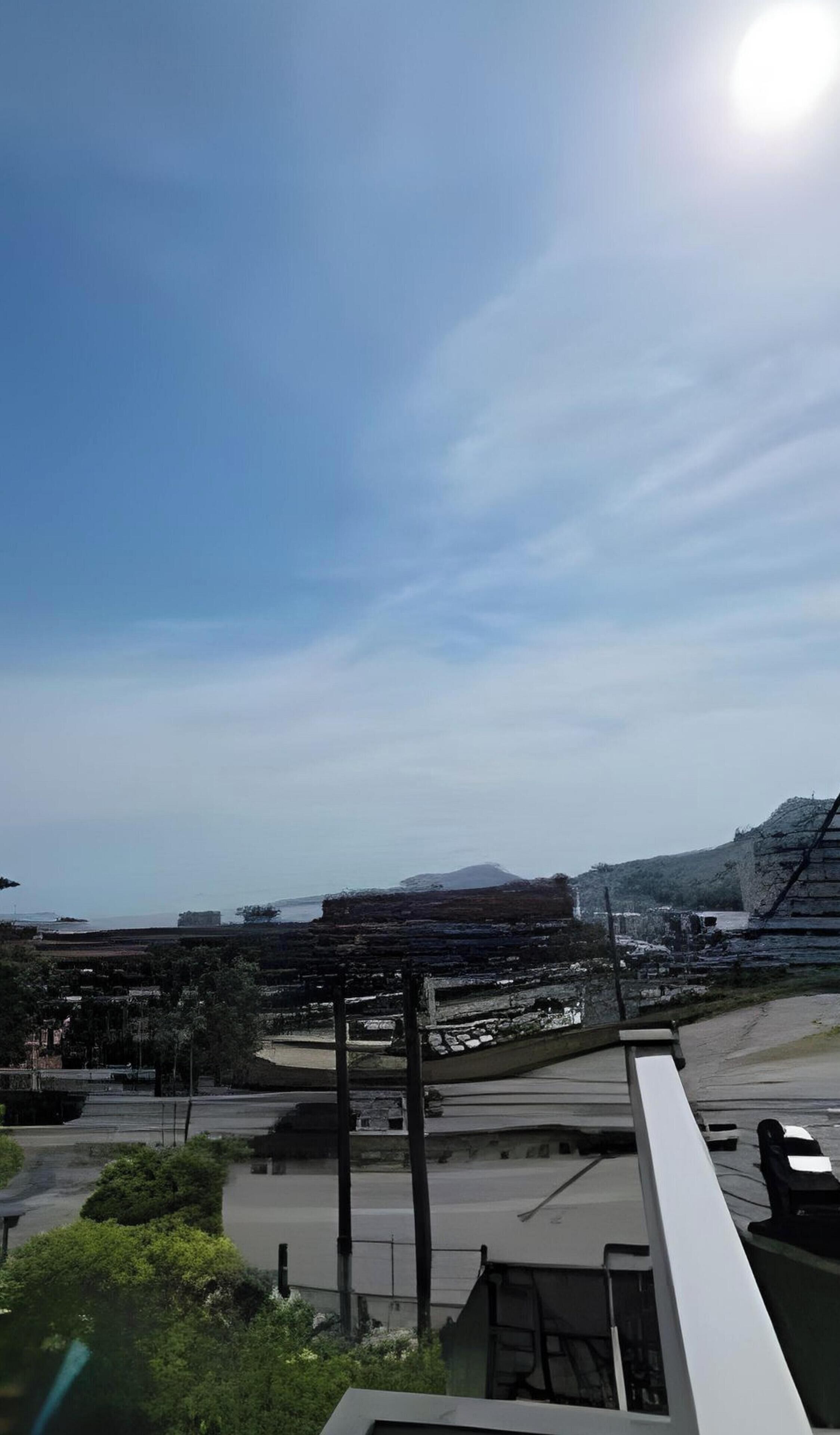 Vista de una zona costera con cielo despejado, una carretera pavimentada y una montaña distante.