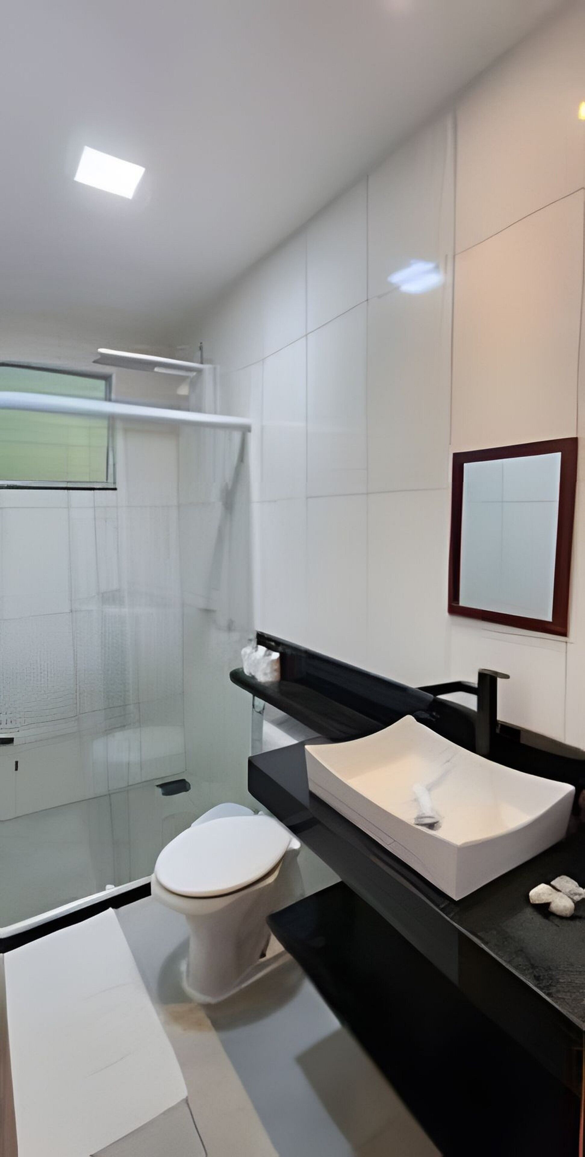 Um banheiro moderno com box de vidro, vaso sanitário branco, pia preta com espelho e uma toalha branca no balcão.