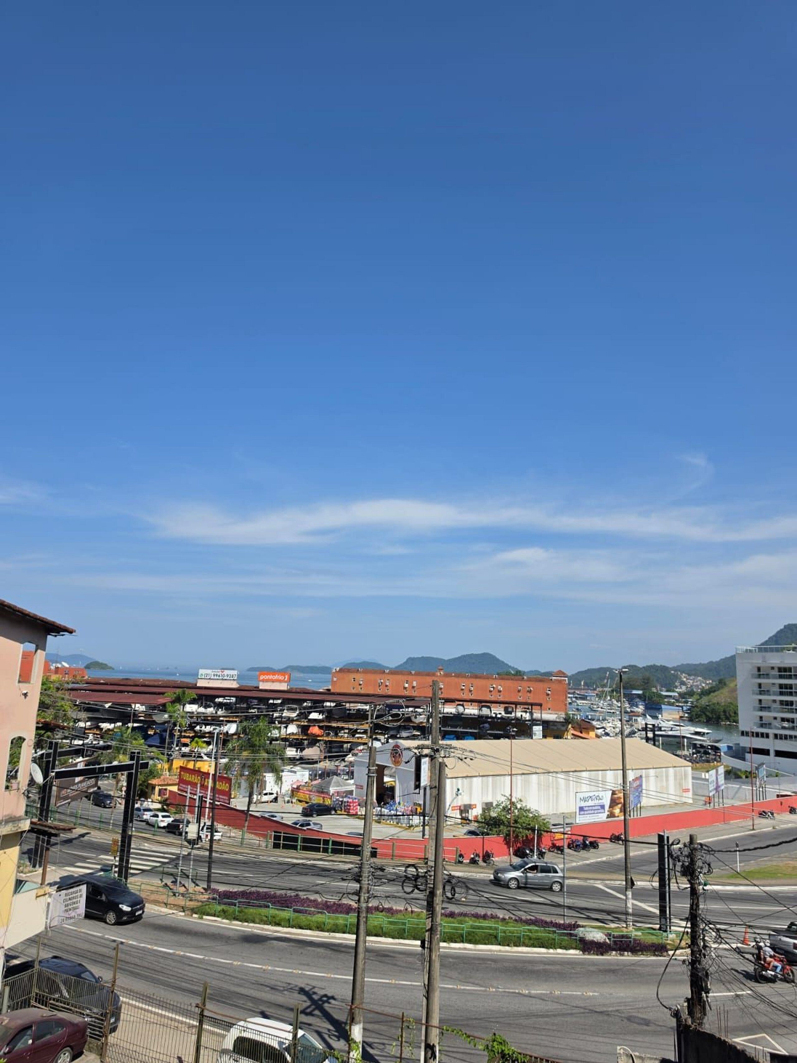 Une rue animée en ville, bordée d’immeubles, avec un ciel dégagé et une vue lointaine sur des collines.