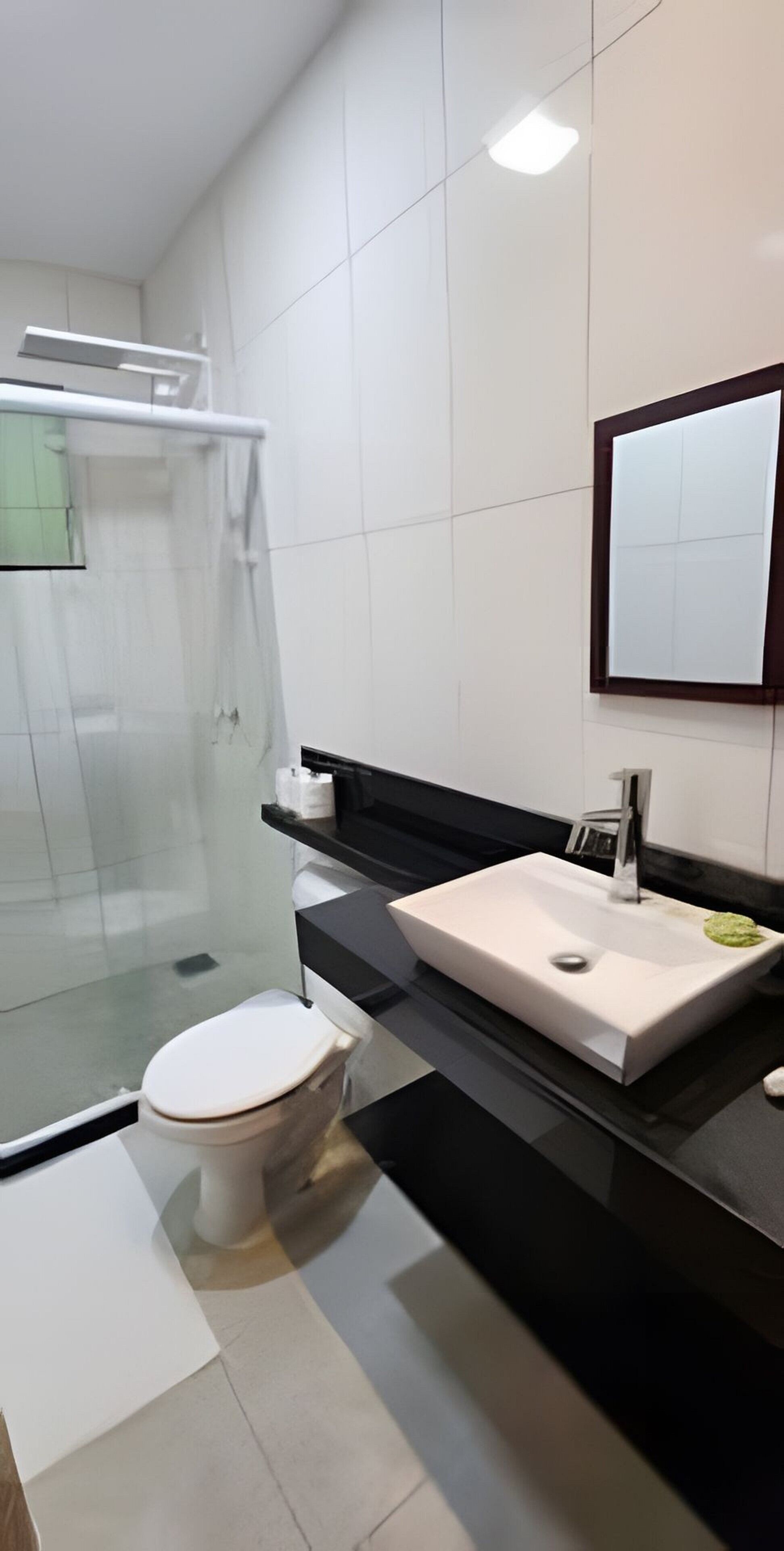 Un baño moderno con cabina de ducha de vidrio, inodoro blanco y encimera negra con lavabo blanco.