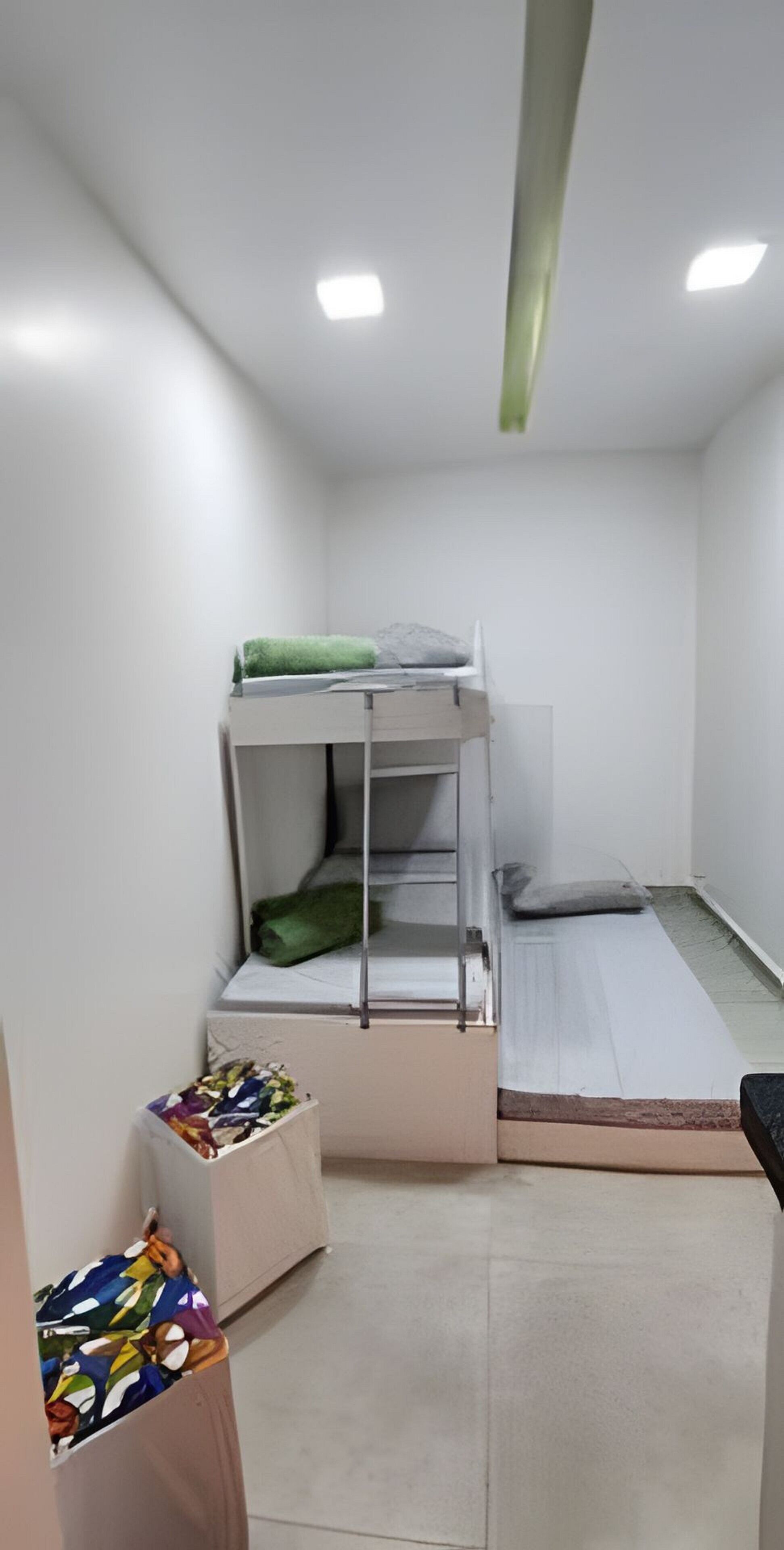 A bunk bed with a green blanket, a small bedside table, and a colorful bag on the floor.