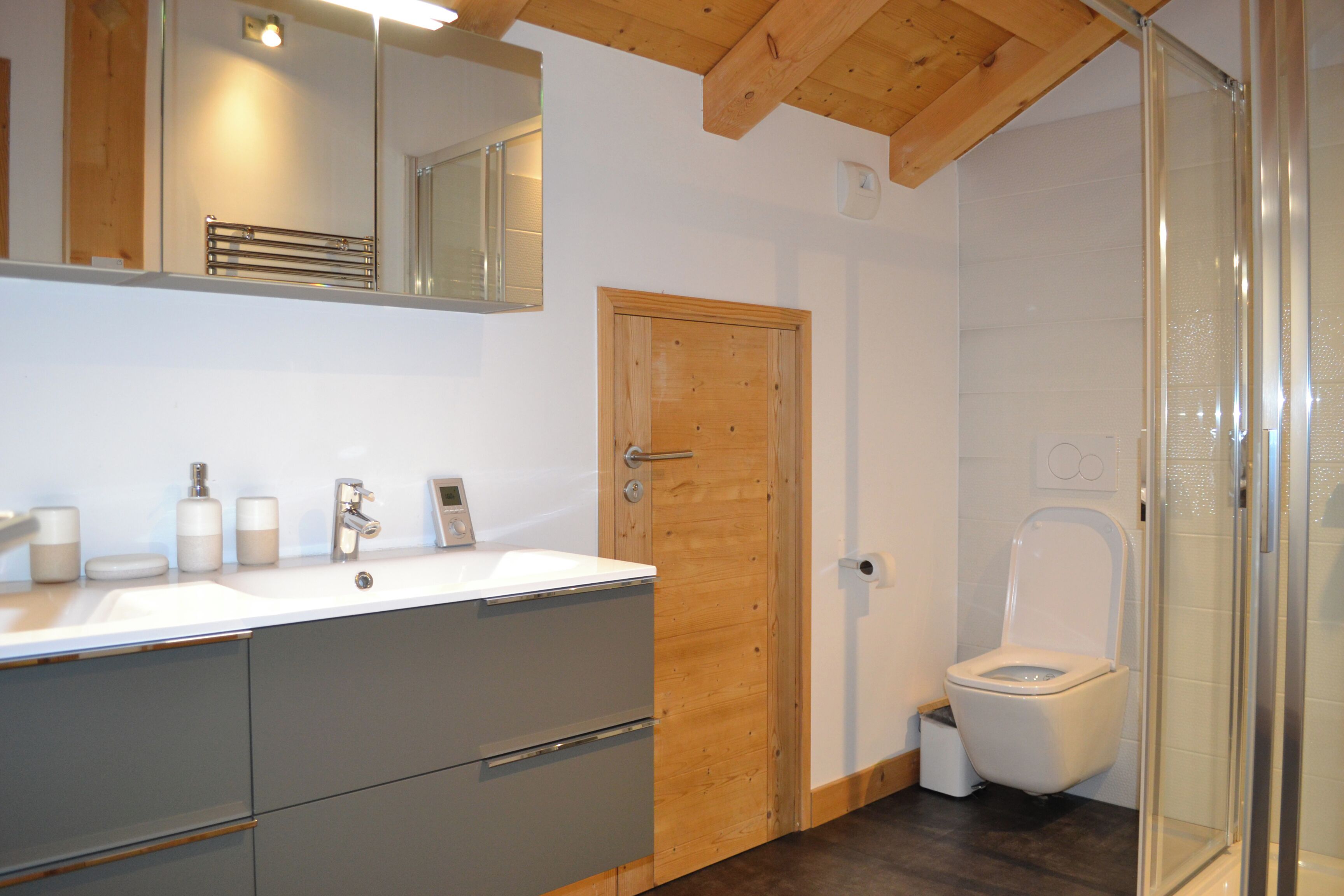 A bathroom with a wooden door, a white sink with a mirror above it, and a toilet with a glass enclosure.